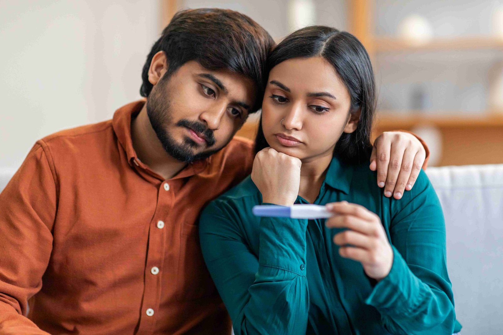 loving indian couple sits close together their living room both intently focused pregnancy 1 11zon scaled